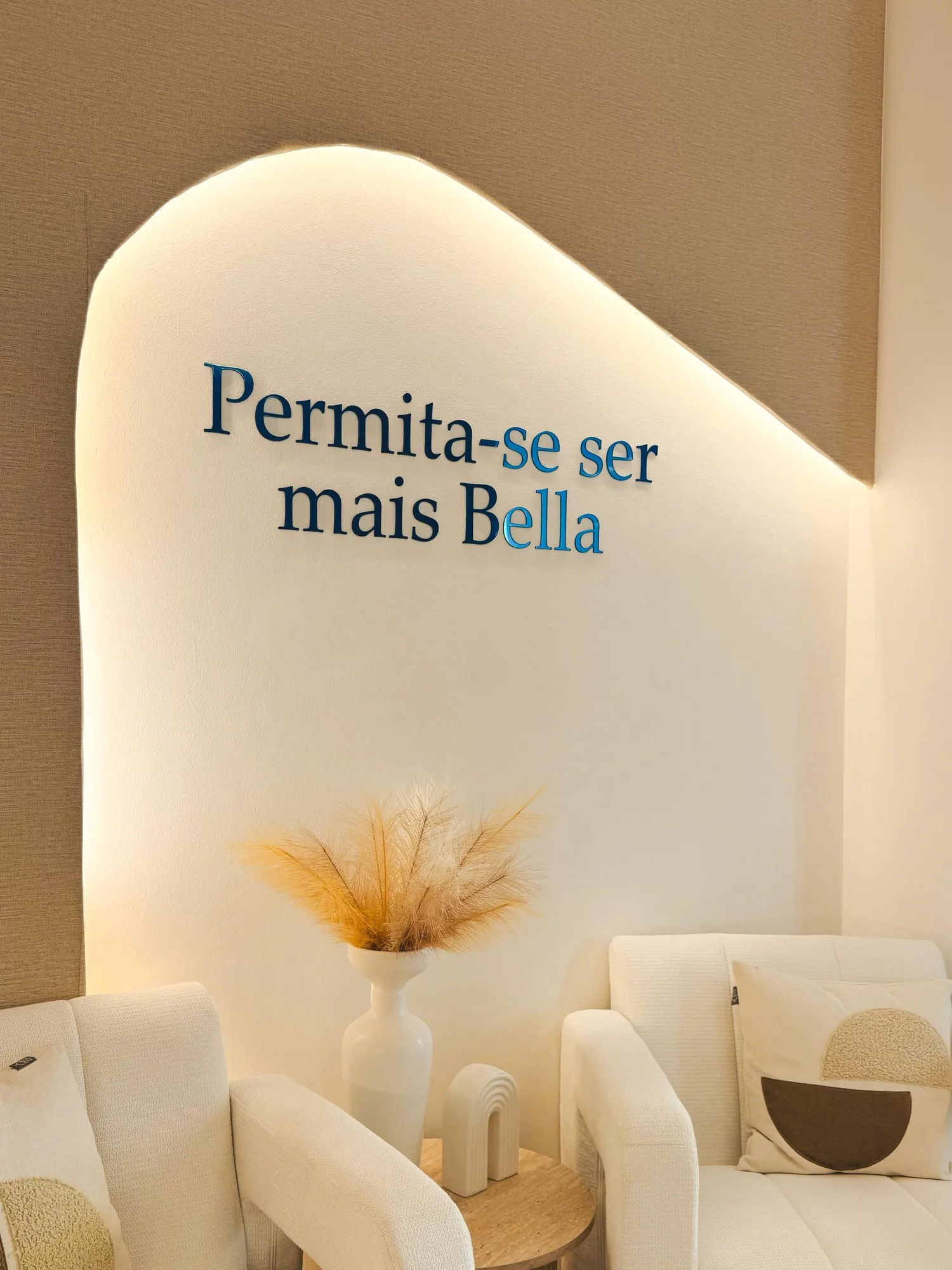 Sala de espera da Bella Laser Clinic, com o nicho retroiluminado onde se lê Permita-se ser mais Bella